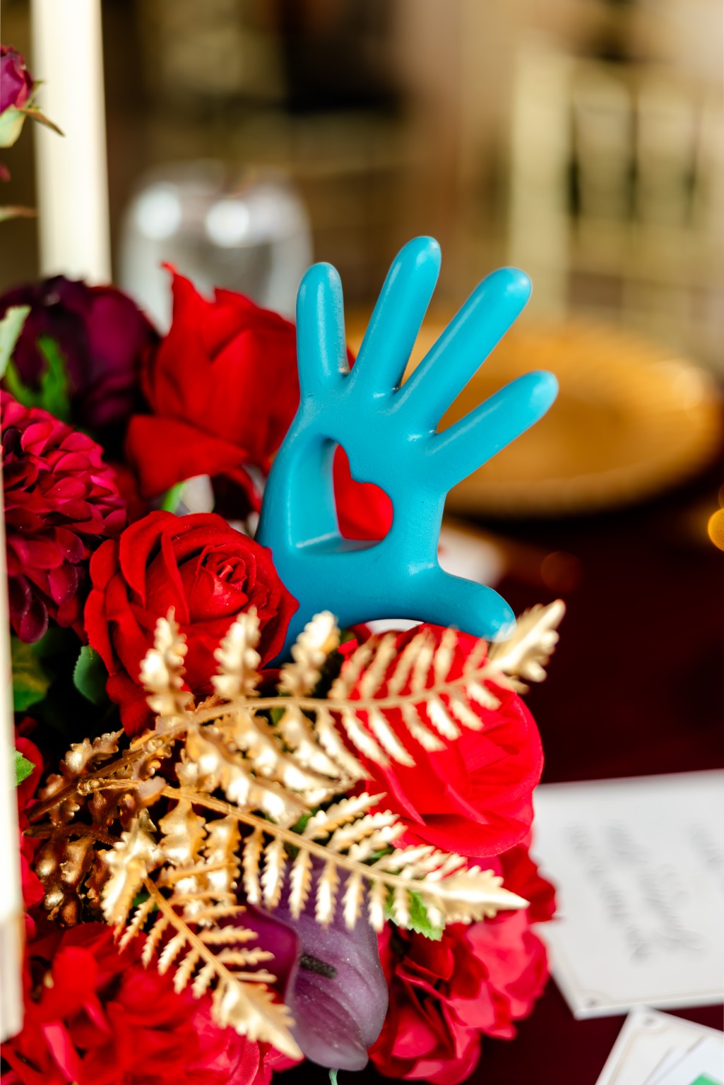 Turquoise hand-shaped decorative piece among red flowers and gold foliage at the 2026 Goodness Gala