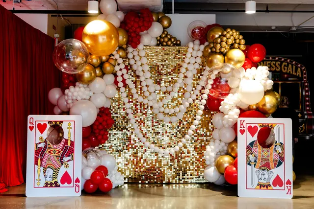 Gold, white and red balloon backdrop with playing-card decor at the 2026 Goodness Gala